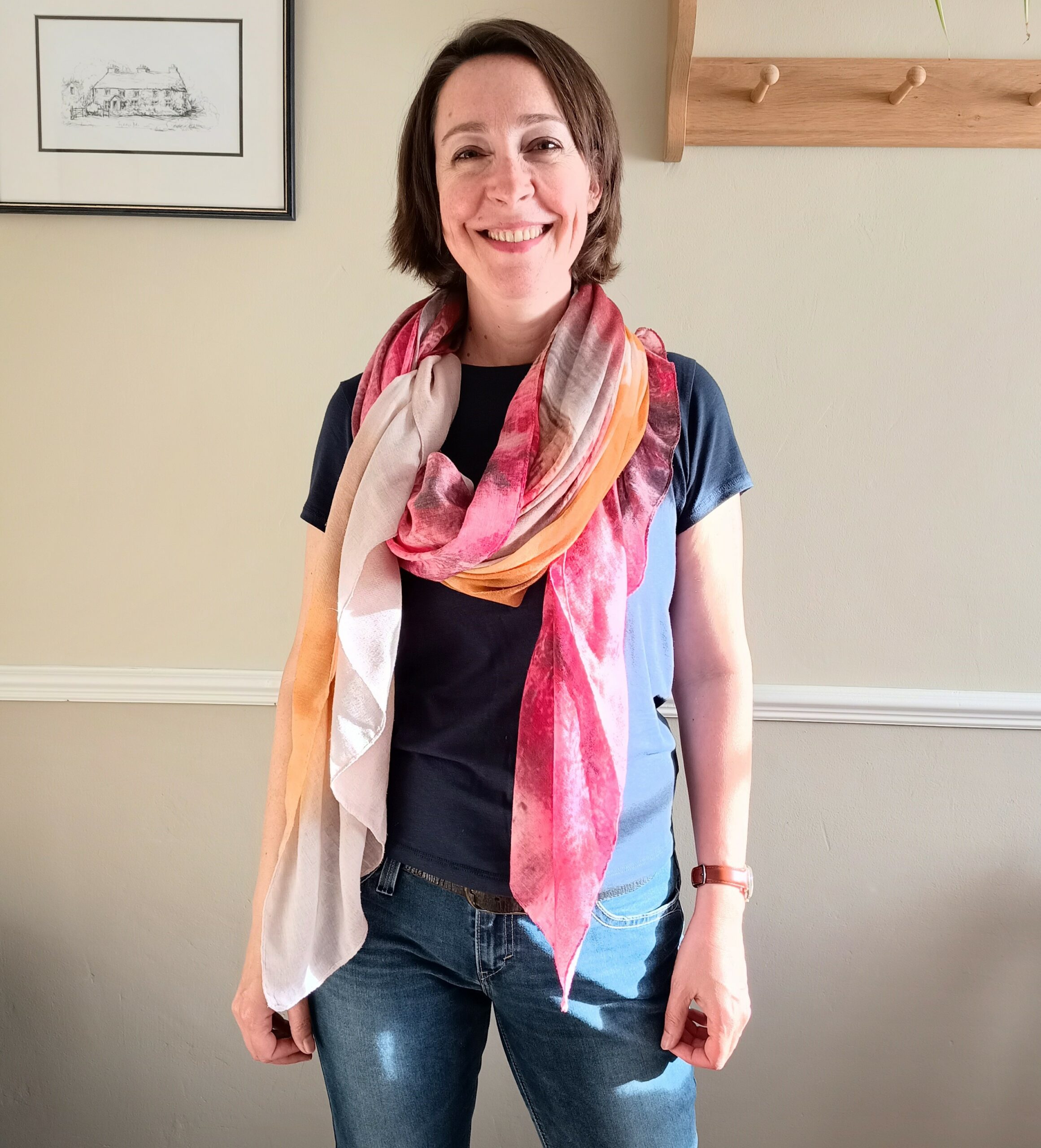 photo of Ingrid Pope, smiling, standing in front of a wall, wearing jeans, a blue t-shirt and a pink scarf